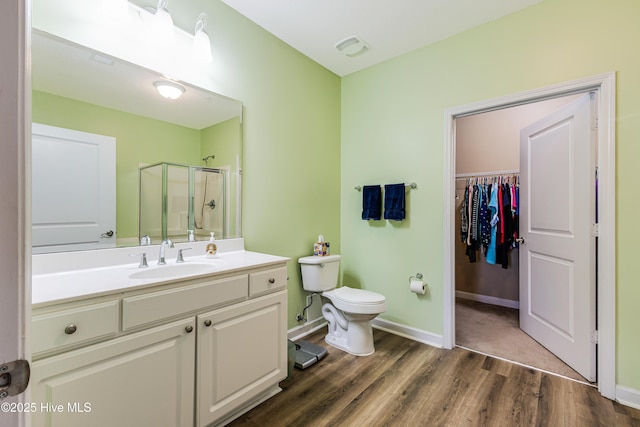 bathroom with toilet, a shower stall, vanity, wood finished floors, and baseboards