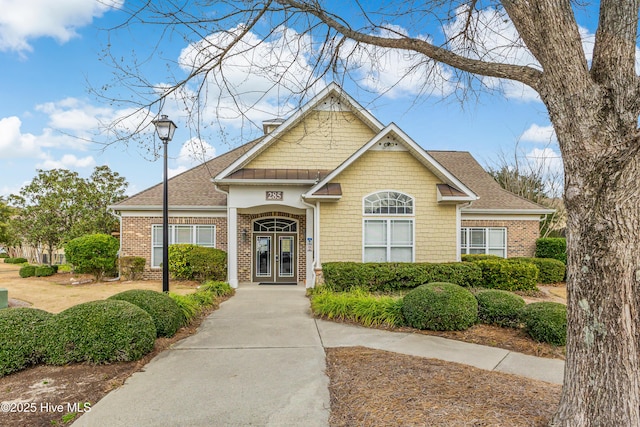 view of front of house featuring brick siding, a shingled roof, a chimney, and french doors