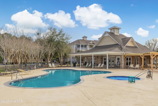 community pool with a patio area, a hot tub, and fence