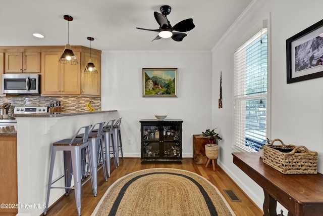 interior space with visible vents, ornamental molding, backsplash, appliances with stainless steel finishes, and a breakfast bar area