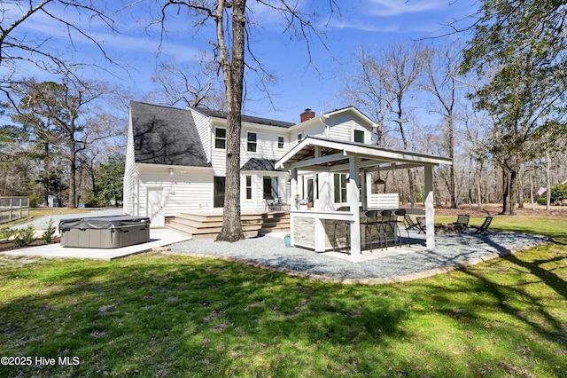 rear view of property featuring a patio, a wooden deck, a chimney, a hot tub, and a lawn