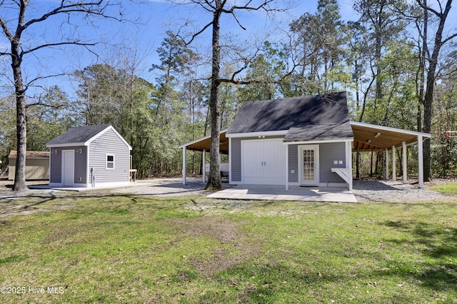 back of house featuring an outdoor structure, a yard, a carport, and roof with shingles