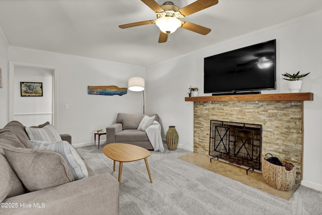 carpeted living room featuring a stone fireplace, crown molding, baseboards, and ceiling fan