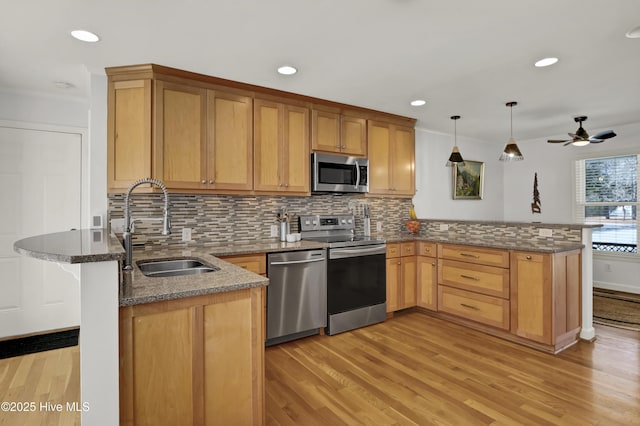 kitchen featuring dark stone countertops, a peninsula, a sink, decorative backsplash, and stainless steel appliances