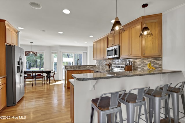 kitchen with light wood-style floors, tasteful backsplash, appliances with stainless steel finishes, and a peninsula