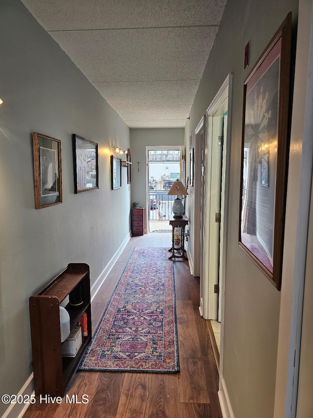 hall featuring a textured ceiling, baseboards, and wood finished floors