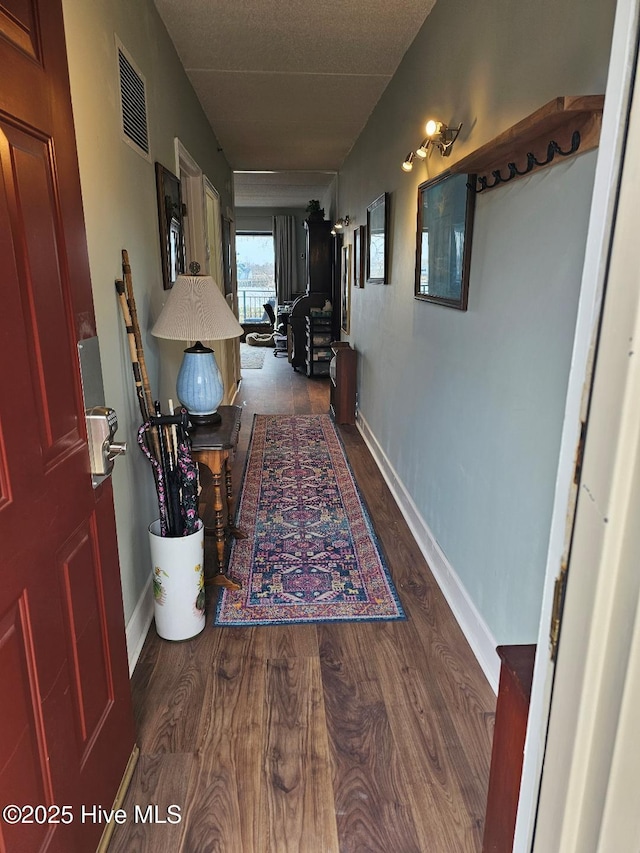 hall with wood finished floors, visible vents, and baseboards