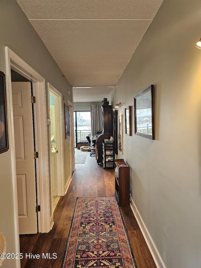 hall with dark wood-type flooring, a textured ceiling, and baseboards