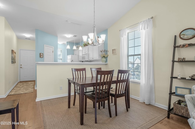 dining room featuring a chandelier, light wood-type flooring, vaulted ceiling, and baseboards