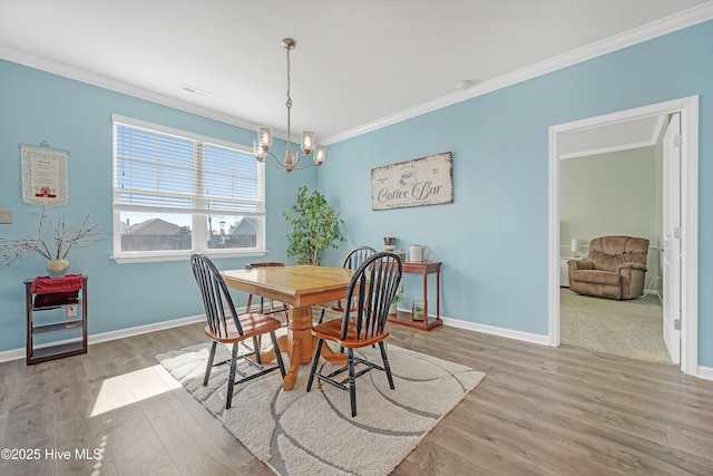 dining space with visible vents, ornamental molding, wood finished floors, baseboards, and a chandelier