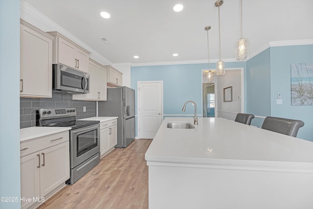 kitchen featuring crown molding, a kitchen island with sink, appliances with stainless steel finishes, and a sink