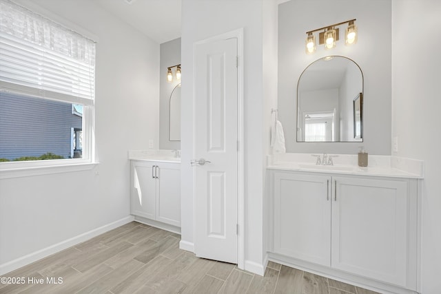 full bath featuring wood finish floors, two vanities, baseboards, and a sink