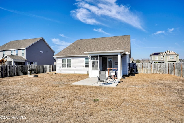 back of house featuring a fenced backyard, a lawn, a shingled roof, and a patio