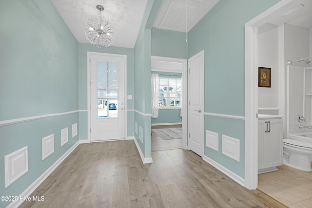 foyer with visible vents, baseboards, light wood-style floors, and a chandelier