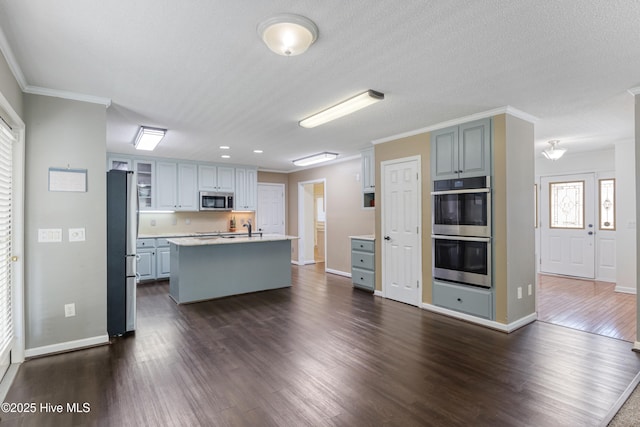 kitchen featuring ornamental molding, a kitchen island with sink, dark wood-style flooring, light countertops, and stainless steel appliances