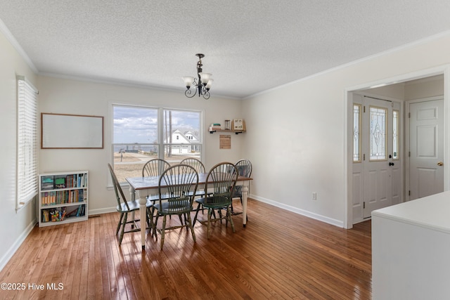 dining space with crown molding, a textured ceiling, a chandelier, wood-type flooring, and baseboards