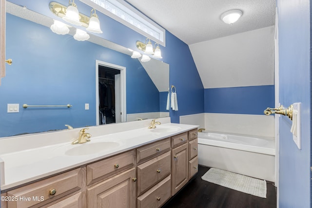 bathroom featuring a bath, a textured ceiling, double vanity, and a sink