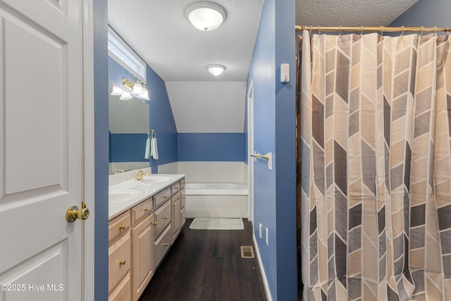 full bath with a garden tub, a textured ceiling, wood finished floors, a sink, and double vanity