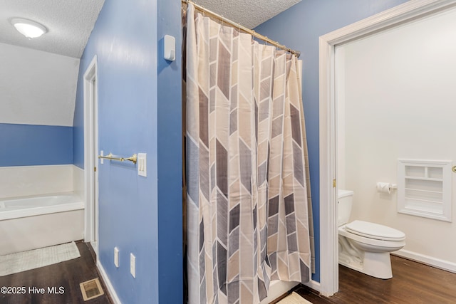 bathroom featuring a textured ceiling, a bath, visible vents, toilet, and wood finished floors