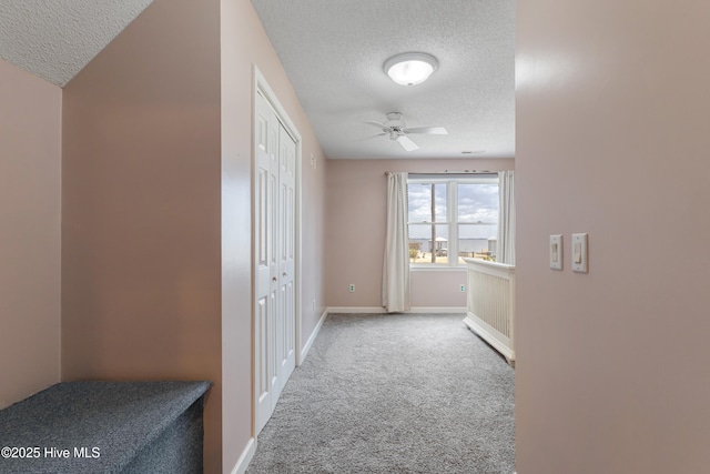 hallway featuring baseboards, carpet, and a textured ceiling