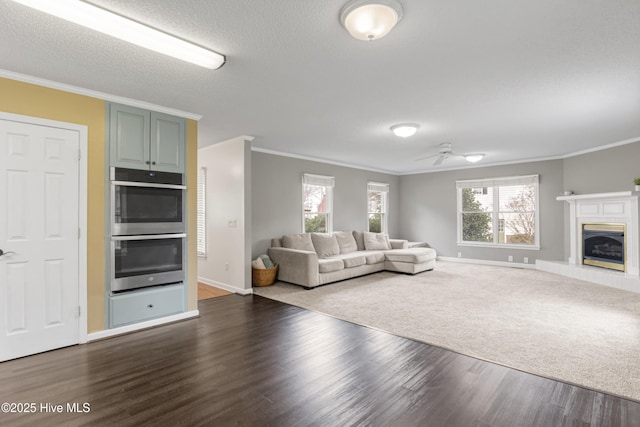 unfurnished living room with crown molding, ceiling fan, a glass covered fireplace, and dark wood-style flooring