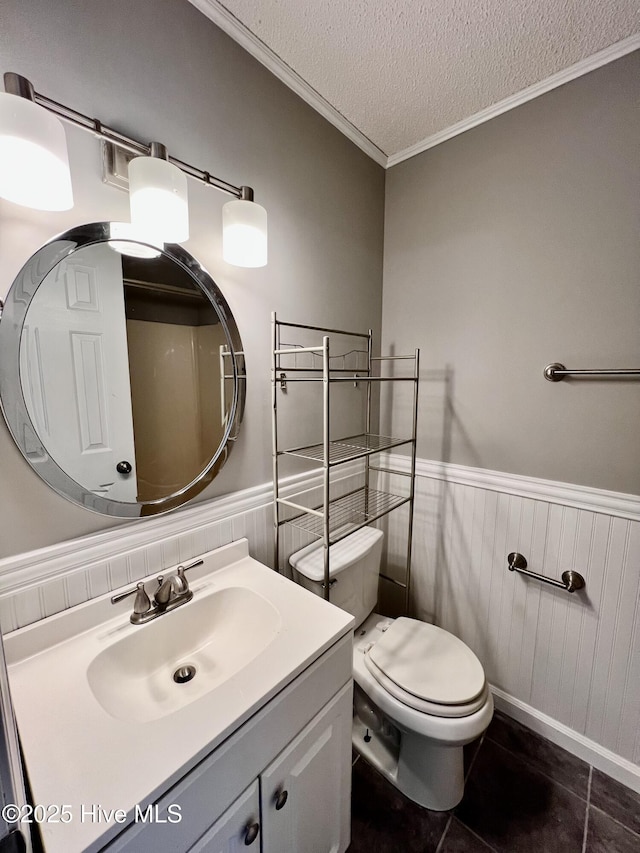 bathroom featuring a textured ceiling, toilet, vanity, ornamental molding, and wainscoting