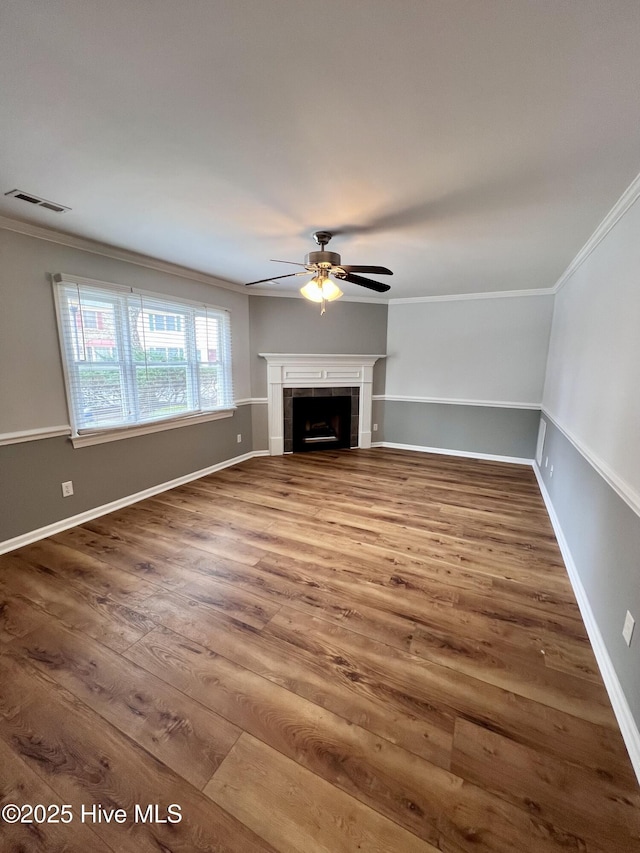 unfurnished living room with ornamental molding, a tiled fireplace, and wood finished floors