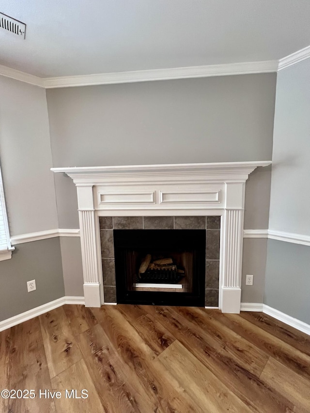 details featuring visible vents, crown molding, a tiled fireplace, and wood finished floors