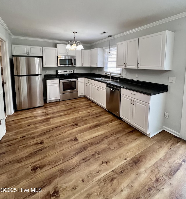 kitchen with dark countertops, appliances with stainless steel finishes, ornamental molding, a sink, and wood finished floors