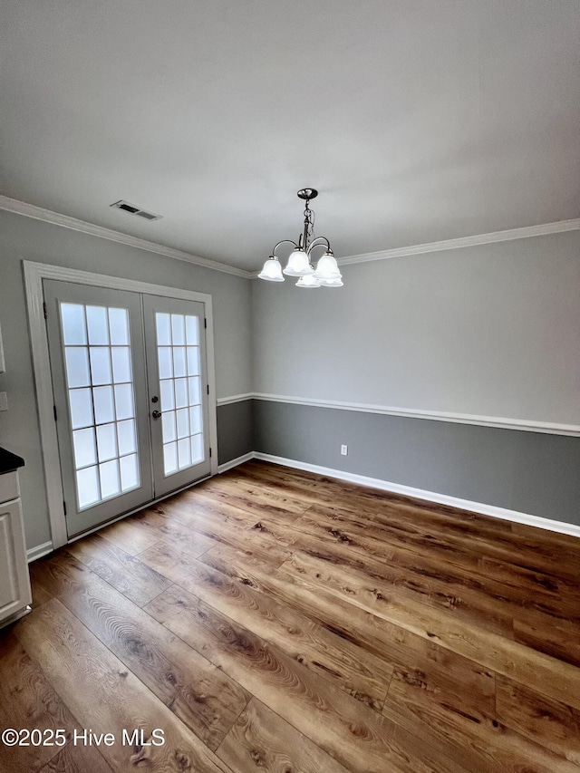 unfurnished dining area with visible vents, ornamental molding, wood finished floors, and french doors