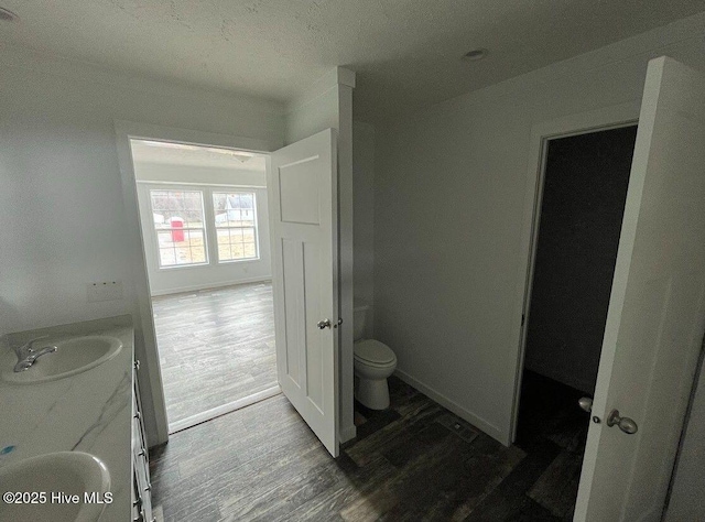 bathroom with double vanity, toilet, a sink, wood finished floors, and baseboards