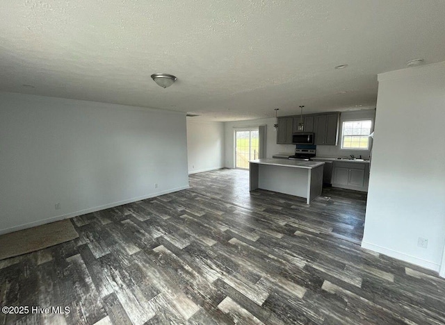 kitchen featuring baseboards, stainless steel appliances, dark wood-type flooring, and open floor plan