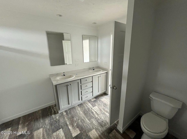 bathroom with double vanity, toilet, a sink, wood finished floors, and baseboards