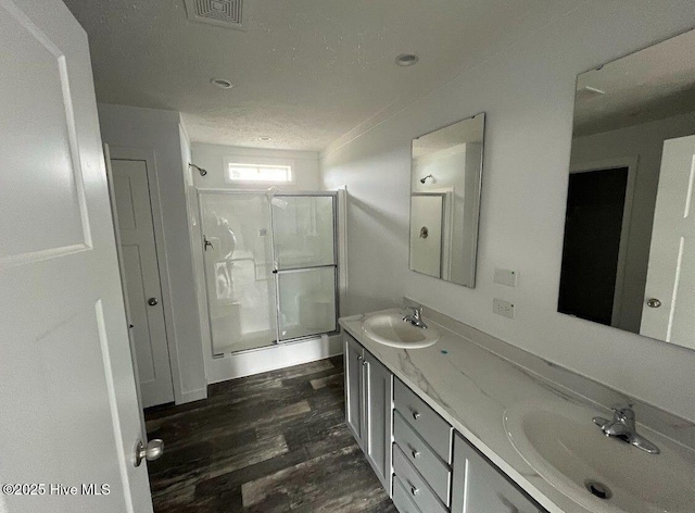 bathroom featuring double vanity, a sink, a shower stall, and wood finished floors