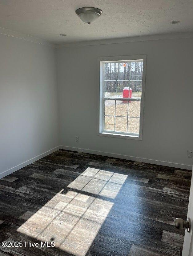 unfurnished room with a textured ceiling, baseboards, wood finished floors, and ornamental molding