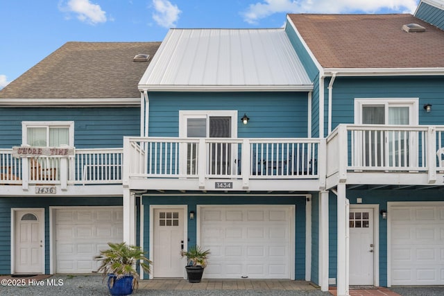 back of property featuring an attached garage, a standing seam roof, a shingled roof, and metal roof