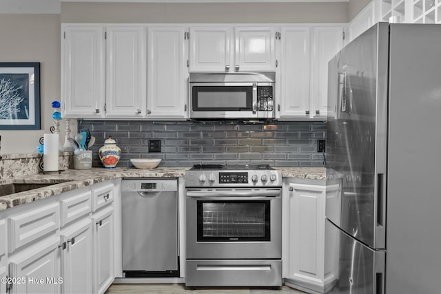 kitchen with stainless steel appliances, a sink, white cabinets, light stone countertops, and tasteful backsplash