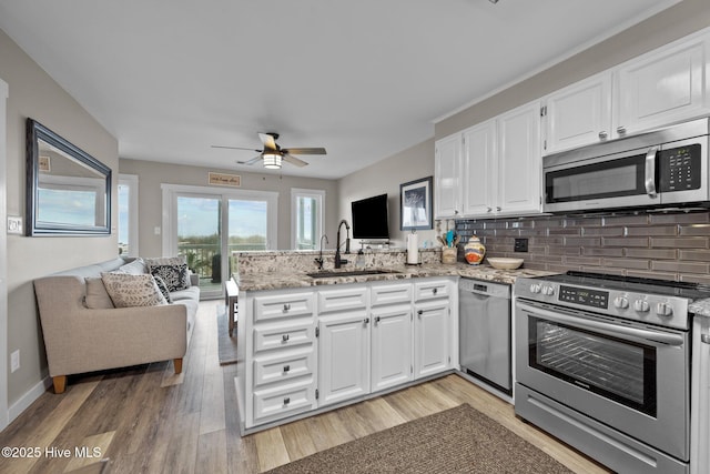 kitchen with stainless steel appliances, a peninsula, a sink, white cabinets, and open floor plan