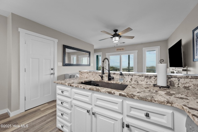 kitchen with light wood-style flooring, a ceiling fan, white cabinetry, a sink, and light stone countertops