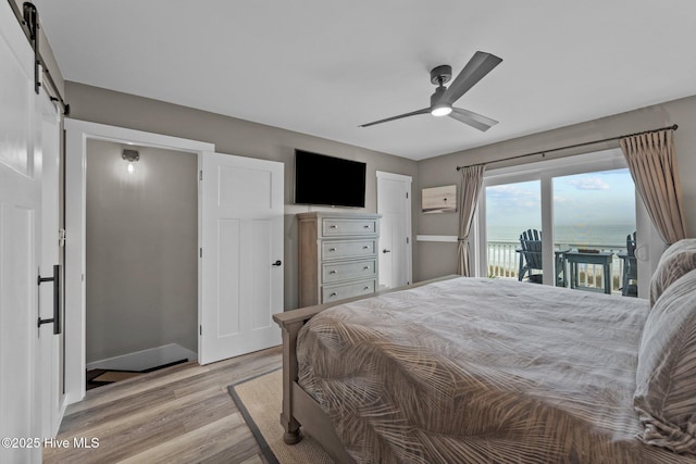 bedroom featuring ceiling fan, a barn door, light wood-style flooring, and access to exterior