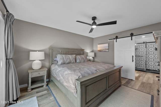 bedroom featuring a barn door, a ceiling fan, light wood-style flooring, and baseboards