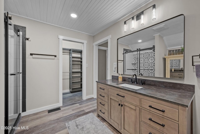 bathroom with baseboards, visible vents, wood finished floors, vanity, and a shower stall