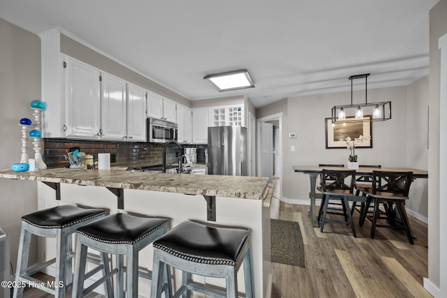 kitchen featuring appliances with stainless steel finishes, wood finished floors, a peninsula, light countertops, and backsplash