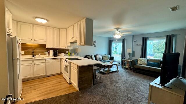 kitchen featuring white appliances, a sink, light countertops, a kitchen bar, and open floor plan