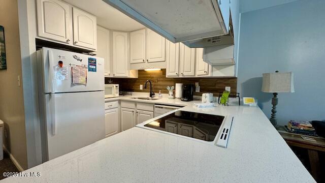 kitchen featuring white appliances, a sink, decorative backsplash, light countertops, and white cabinets