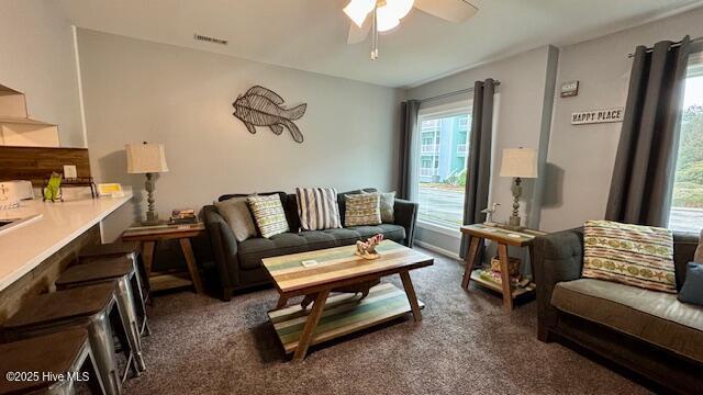 living area featuring a ceiling fan, visible vents, and dark carpet