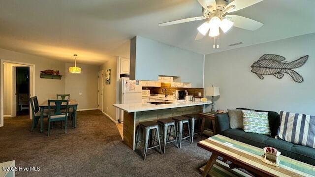 kitchen featuring dark carpet, a breakfast bar, light countertops, a peninsula, and freestanding refrigerator