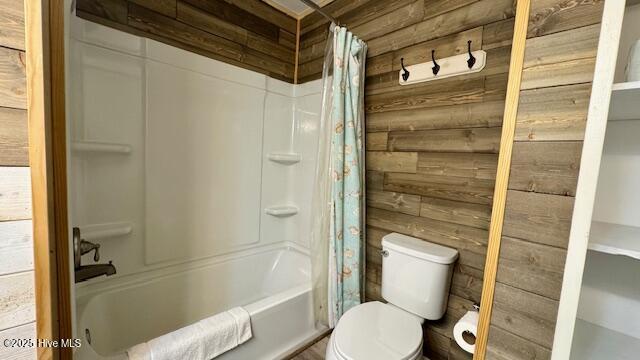 bathroom featuring toilet, shower / bathtub combination with curtain, and wood walls