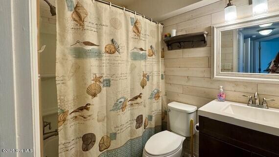 full bath featuring vanity, wooden walls, toilet, and curtained shower