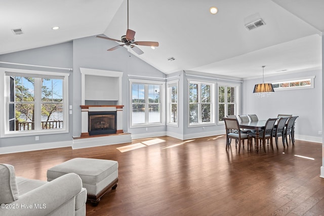 living room featuring dark wood finished floors, visible vents, a fireplace with raised hearth, and ceiling fan